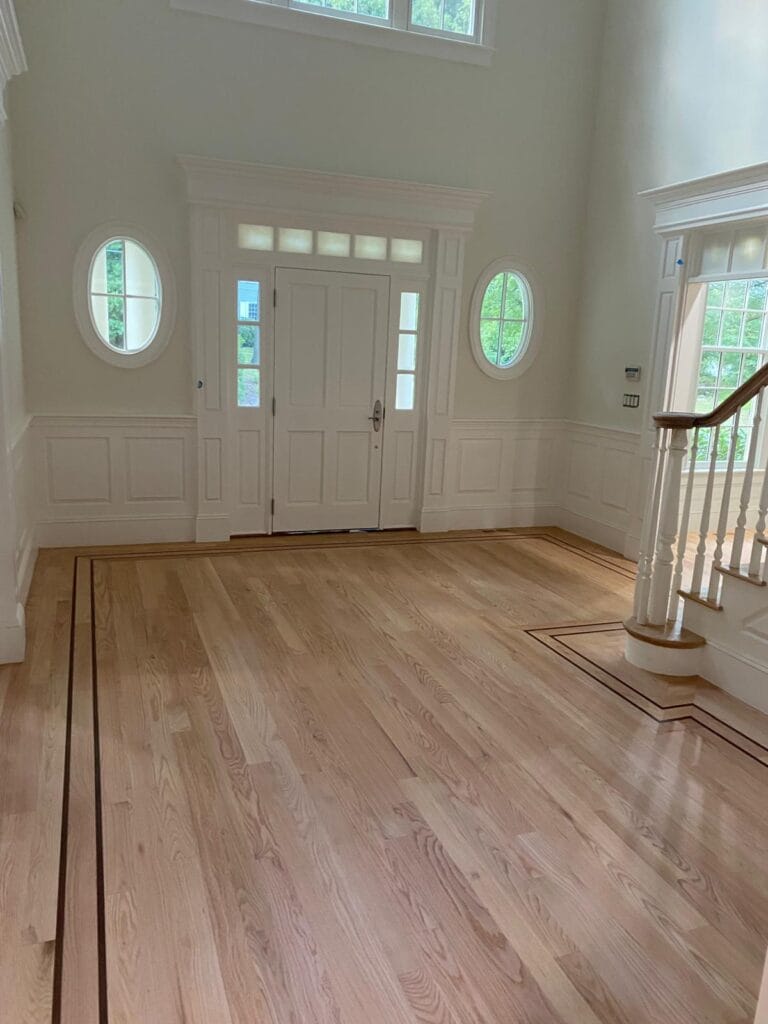 Bright entrance hall featuring newly installed hardwood flooring, elegant white paneling, and decorative oval windows, showcasing GB Hardwood Flooring INC's craftsmanship.